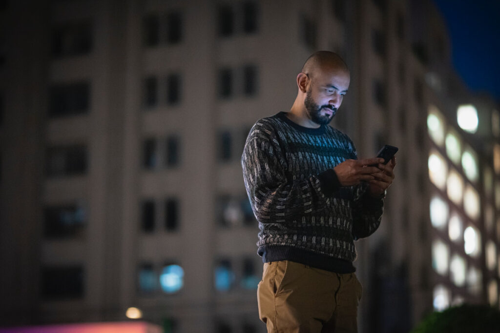 Un hombre sostiene su smartphone en la calle de noche.