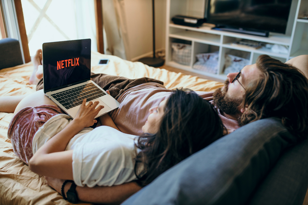 Dos personas ven Netflix en una laptop mientras están acostadas en la cama.